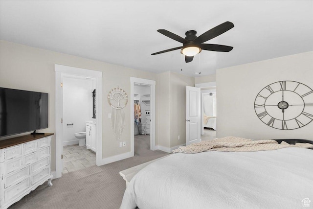 bedroom with a ceiling fan, a spacious closet, connected bathroom, light carpet, and baseboards