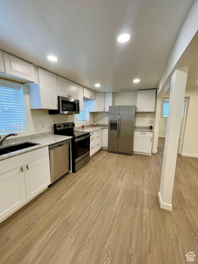 kitchen with appliances with stainless steel finishes, light wood-style floors, white cabinets, a sink, and recessed lighting