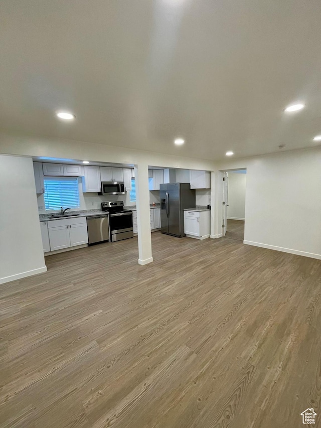 below grade area featuring stainless steel fridge with ice dispenser, a sink, light wood finished floors, baseboards, and recessed lighting