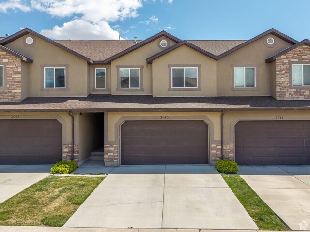 view of property with a garage, stone siding, stucco siding, and a shingled roof