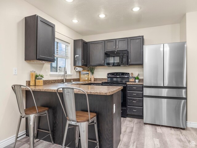 2046 N Belmont Dr, Saratoga Springs, UT 84045 - kitchen with a sink, black appliances, a breakfast bar, light wood-type flooring, and a peninsula