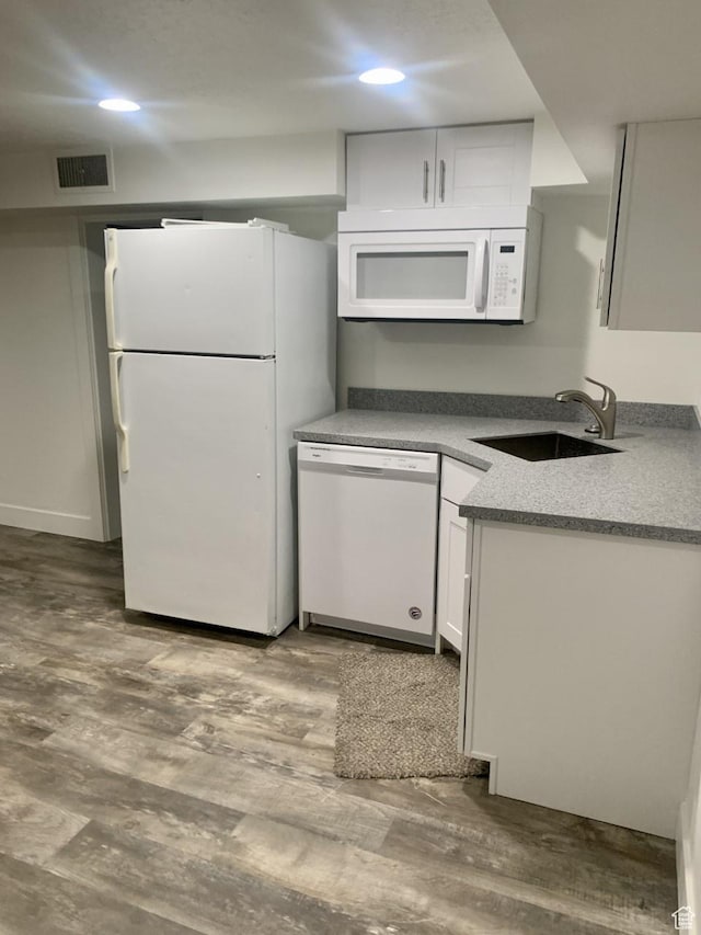 kitchen with a sink, visible vents, white cabinetry, wood finished floors, and white appliances