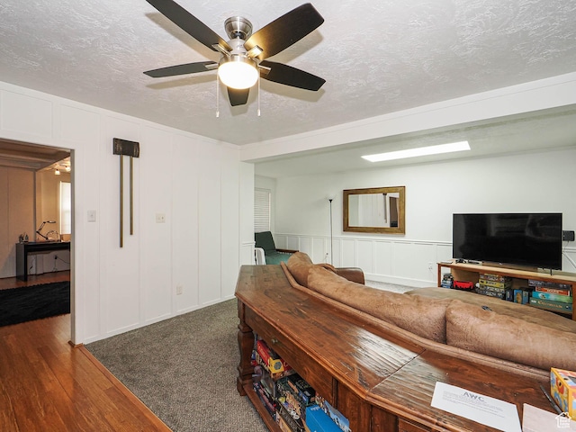 living area with wood finished floors, a textured ceiling, ceiling fan, and a decorative wall