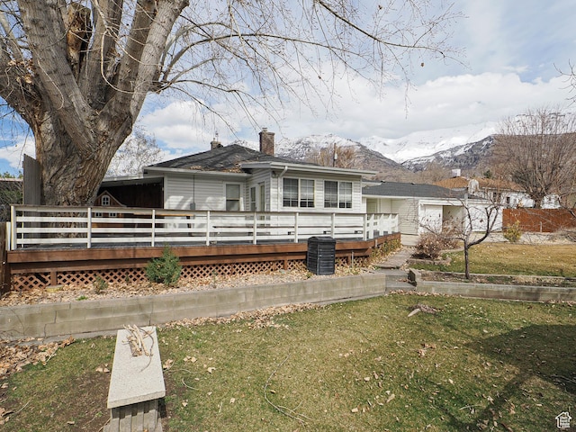 rear view of house with a chimney, a deck with mountain view, and a lawn