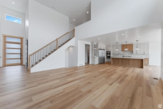 3010 W Willow Dr S, Lehi, UT 84043 - unfurnished living room with light wood-style floors, visible vents, stairs, and a towering ceiling