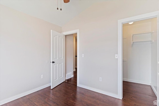 unfurnished bedroom with a spacious closet, vaulted ceiling, wood finished floors, a closet, and baseboards