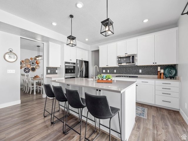 1058 S 800 W, American Fork, UT 84003 - kitchen featuring white cabinets, a center island with sink, decorative backsplash, a breakfast bar, and appliances with stainless steel finishes