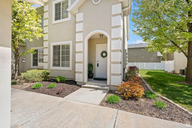 doorway to property with a lawn, stucco siding, and fence