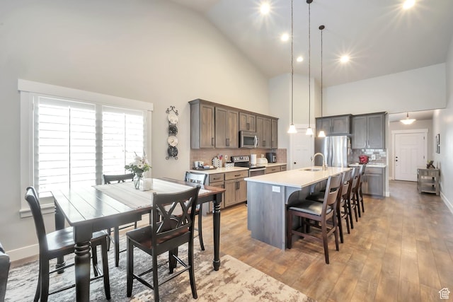 kitchen featuring a sink, a breakfast bar, high vaulted ceiling, an island with sink, and appliances with stainless steel finishes