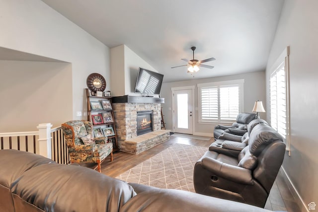 living area featuring lofted ceiling, a stone fireplace, wood finished floors, a ceiling fan, and baseboards