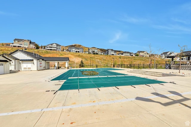 community pool with a patio area, fence, and a residential view