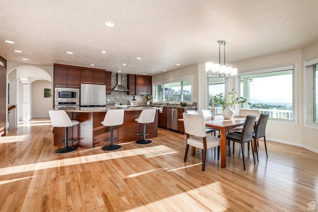 dining space featuring arched walkways, light wood finished floors, and recessed lighting