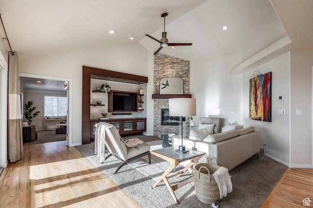 living area with wood finished floors, a ceiling fan, baseboards, a fireplace, and high vaulted ceiling