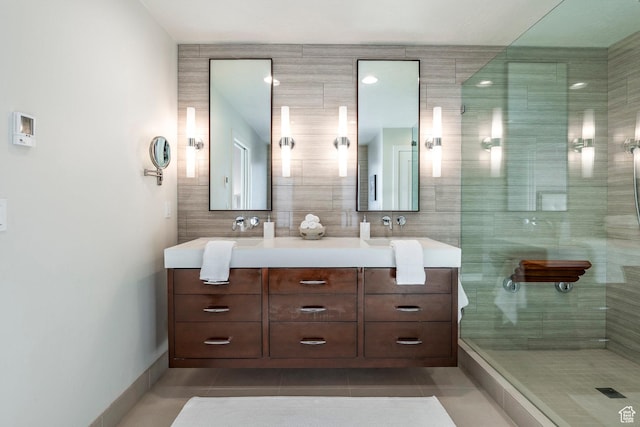 bathroom featuring a tile shower, baseboards, tile patterned flooring, and double vanity
