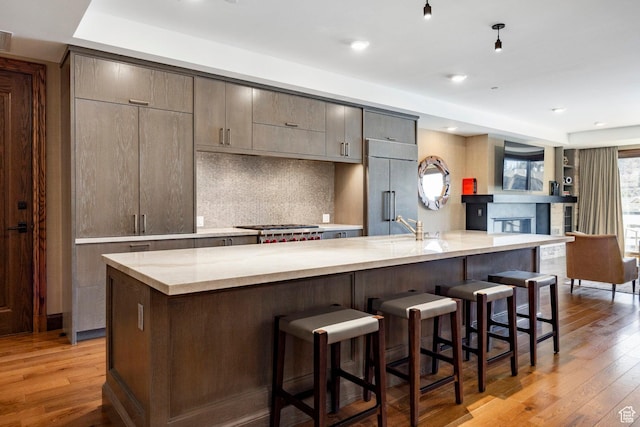 kitchen featuring built in refrigerator, light stone countertops, light wood-style flooring, tasteful backsplash, and a breakfast bar area