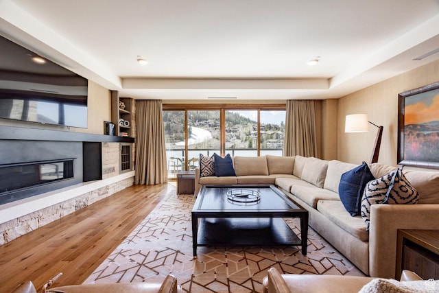 living room featuring a stone fireplace, wood finished floors, and built in features