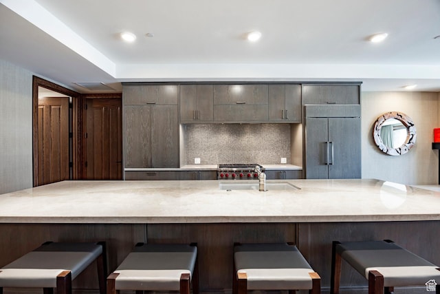kitchen with a kitchen breakfast bar, light stone counters, backsplash, a sink, and built in fridge