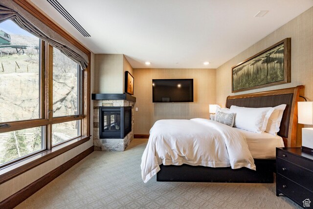 bedroom featuring light colored carpet, baseboards, multiple windows, and a multi sided fireplace