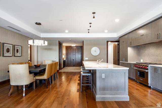 kitchen featuring a kitchen breakfast bar, light countertops, designer stove, light wood-type flooring, and a kitchen island with sink