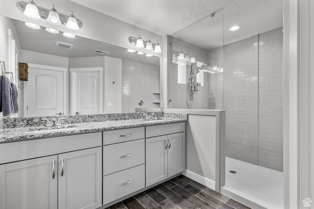 bathroom with a textured ceiling, a sink, walk in shower, double vanity, and visible vents