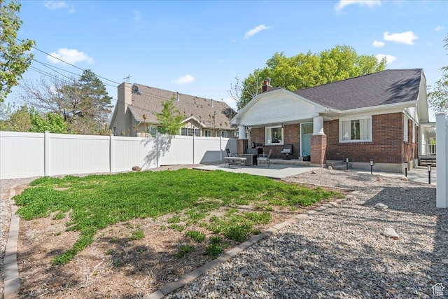 rear view of property featuring a patio area, a chimney, a lawn, a fenced backyard, and brick siding