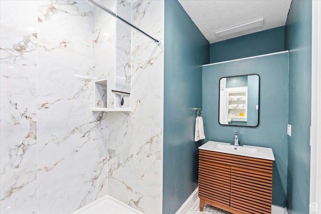 full bath with a tile shower, baseboards, vanity, and a textured ceiling