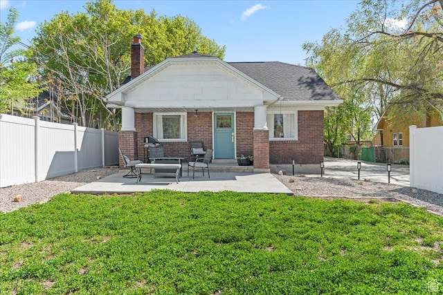 back of house featuring a lawn, a chimney, brick siding, and fence private yard