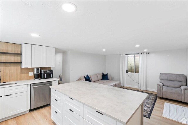 kitchen featuring light wood finished floors, open floor plan, stainless steel dishwasher, and light countertops