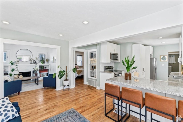 kitchen featuring white cabinets, a kitchen breakfast bar, light wood-style floors, light stone countertops, and appliances with stainless steel finishes