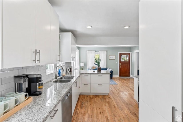 kitchen featuring stainless steel dishwasher, a sink, light wood-style floors, a peninsula, and white cabinetry