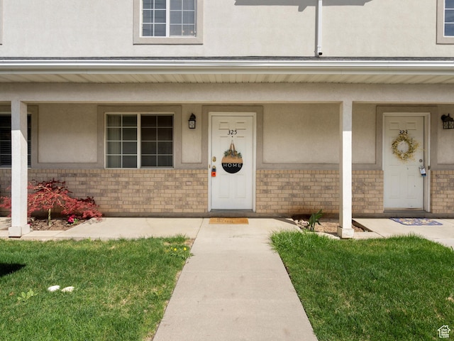 view of exterior entry featuring a porch, brick siding, and stucco siding