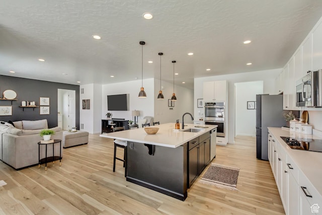 kitchen with open floor plan, stainless steel appliances, light wood finished floors, and a sink