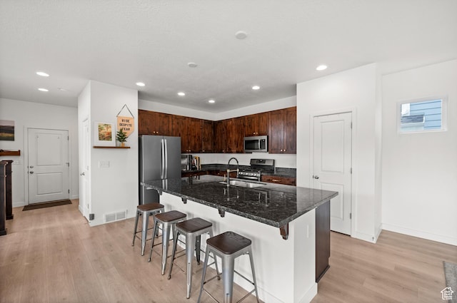 kitchen with light wood-type flooring, stainless steel appliances, a kitchen bar, visible vents, and recessed lighting