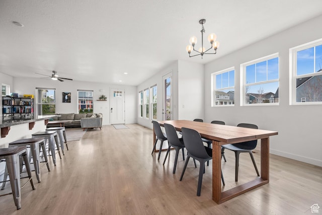 dining area with light wood-style floors, baseboards, and ceiling fan with notable chandelier