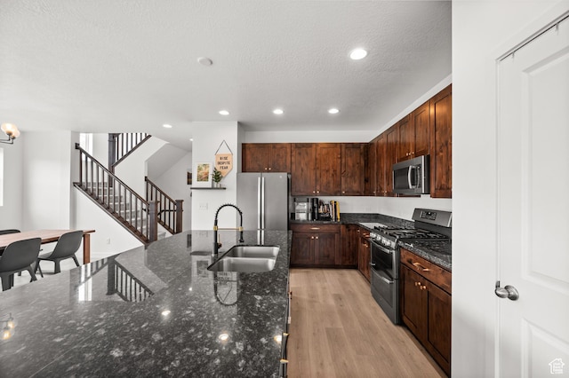 kitchen with dark stone counters, a textured ceiling, a sink, stainless steel appliances, and light wood finished floors