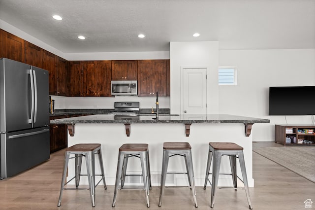 kitchen with light wood-style flooring, a sink, dark stone countertops, a breakfast bar, and appliances with stainless steel finishes