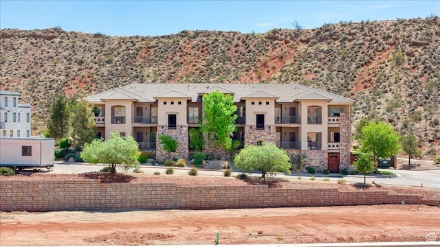 view of front of house with stone siding, a balcony, a mountain view, and stucco siding