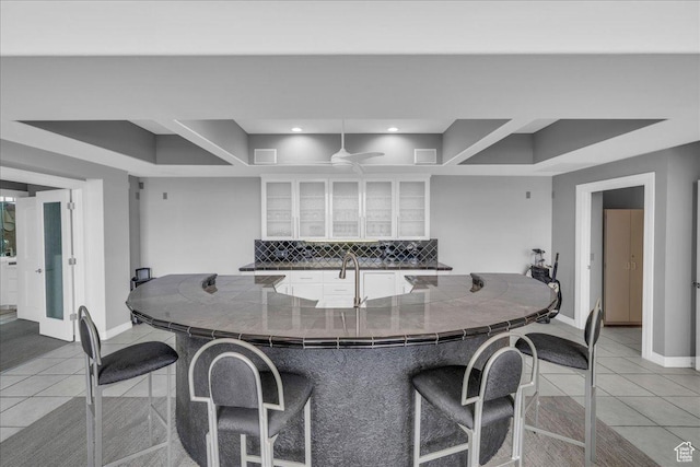 kitchen featuring light tile patterned flooring, decorative backsplash, a kitchen breakfast bar, and white cabinetry