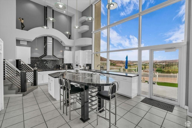 kitchen featuring wall chimney exhaust hood, dark countertops, a towering ceiling, and floor to ceiling windows