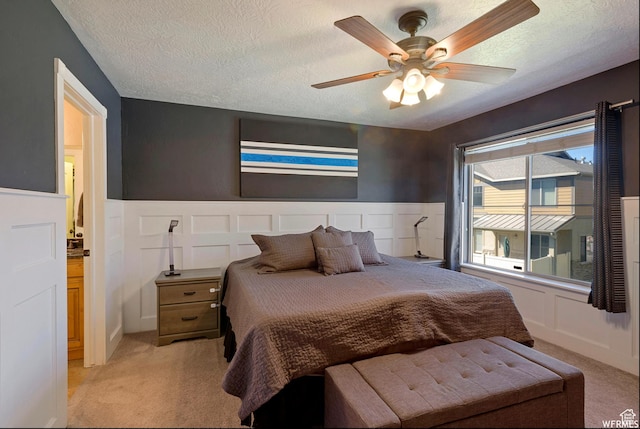 bedroom with light colored carpet, wainscoting, and a textured ceiling