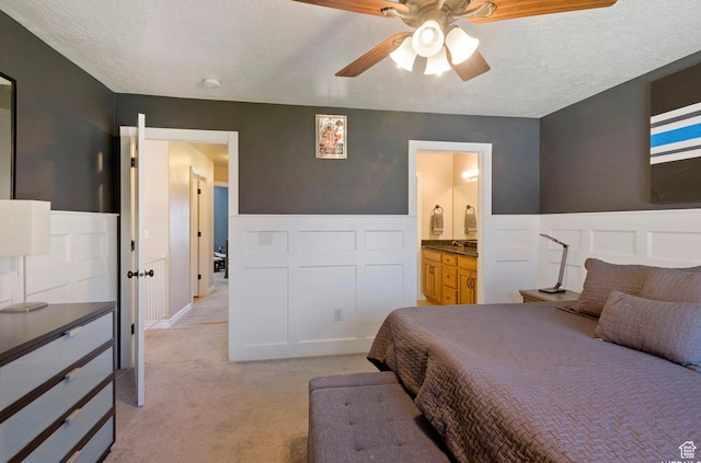 bedroom with wainscoting, light carpet, a textured ceiling, and connected bathroom