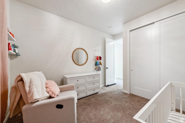 carpeted bedroom featuring baseboards, a crib, a textured ceiling, and a closet