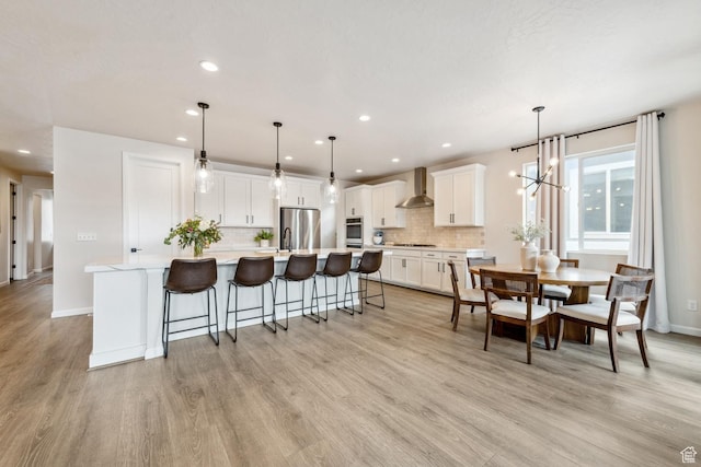 kitchen featuring wall chimney range hood, appliances with stainless steel finishes, tasteful backsplash, and light wood finished floors