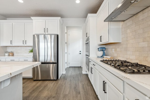 kitchen with wall chimney exhaust hood, white cabinets, backsplash, and appliances with stainless steel finishes
