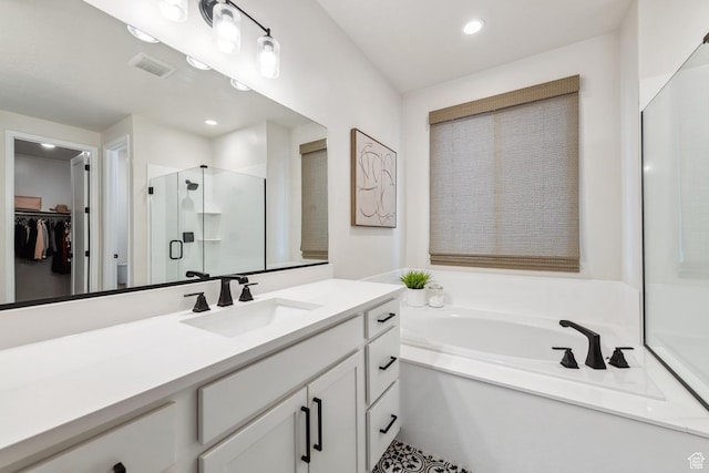 bathroom featuring visible vents, a spacious closet, a shower stall, a garden tub, and vanity