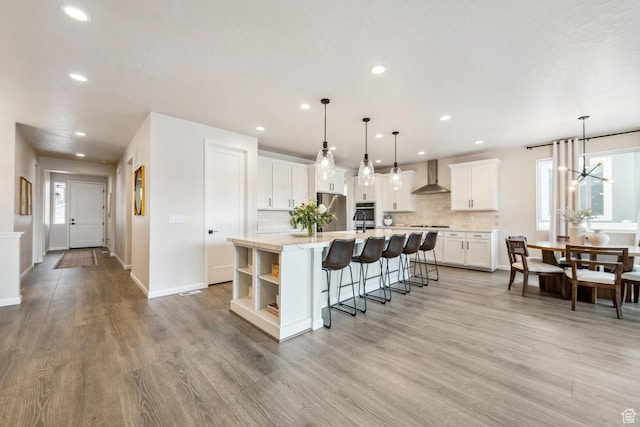 kitchen featuring stainless steel appliances, a large island with sink, decorative backsplash, wall chimney range hood, and light countertops