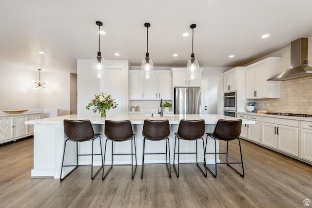 kitchen featuring wall chimney range hood, tasteful backsplash, wood finished floors, a kitchen island with sink, and freestanding refrigerator