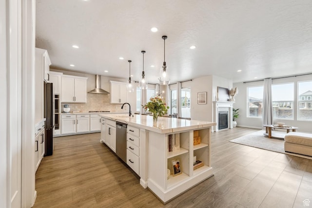 kitchen with wall chimney range hood, a spacious island, open floor plan, stainless steel appliances, and recessed lighting