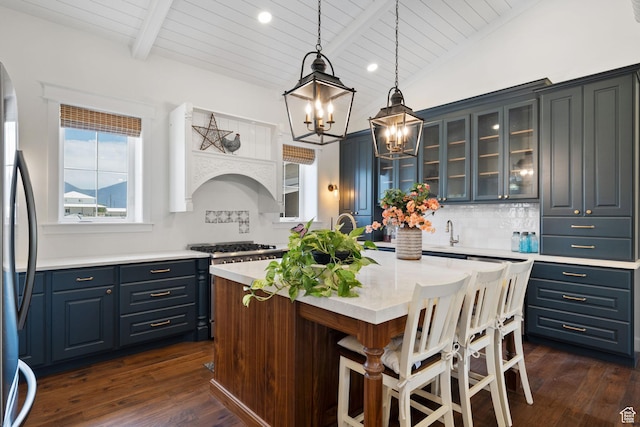 kitchen with dark wood-style floors, a center island with sink, an inviting chandelier, stainless steel refrigerator, and a breakfast bar