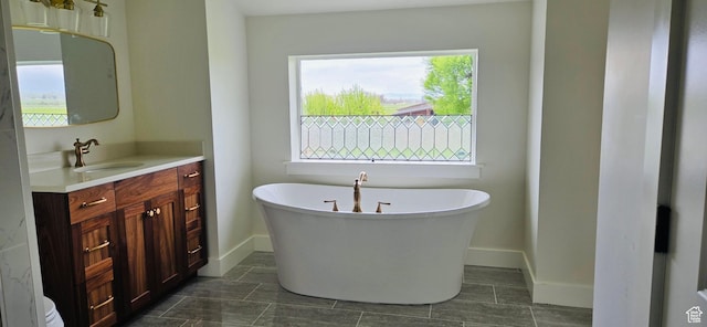 full bath with vanity, a freestanding tub, and baseboards